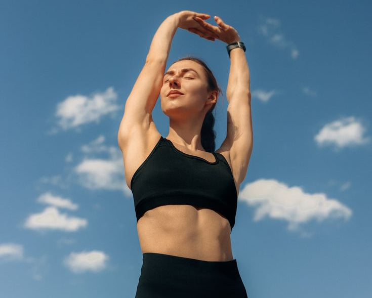 Woman in black athletic wear stretching against a blue sky with scattered clouds