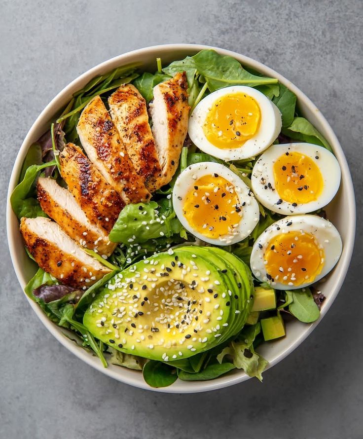 Salad with chicken, boiled eggs, and avocado in a white bowl on a gray background